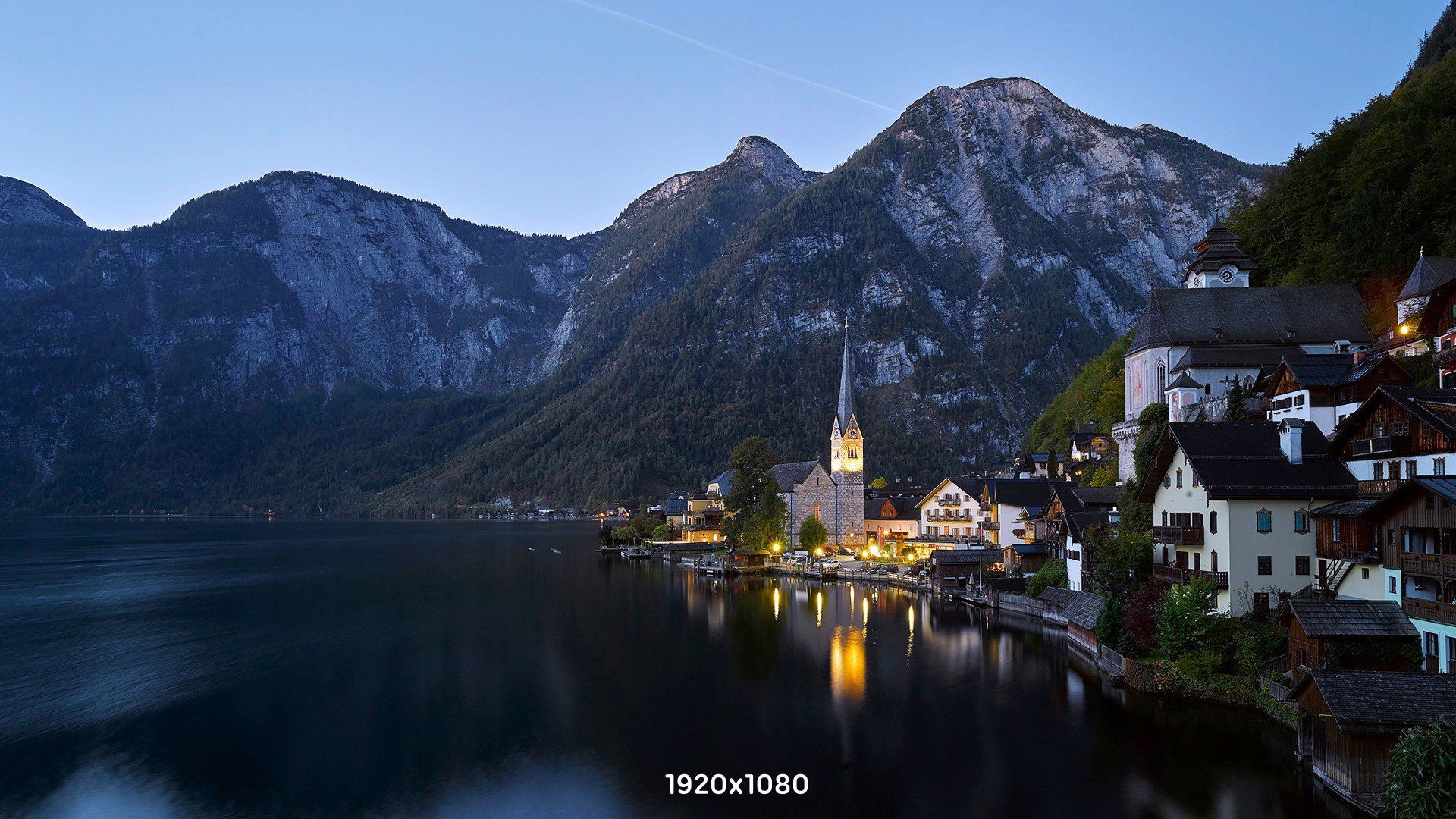 Panorama di Hallstatt. Un lago circondato da montagne su cui si affaccia un paesino con una chiesa illuminata